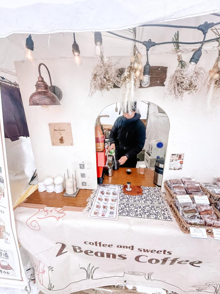 Cozy Beans Coffee pop-up stall with hanging dried flowers and warm Edison bulbs at Asahikawa Winter Festival.