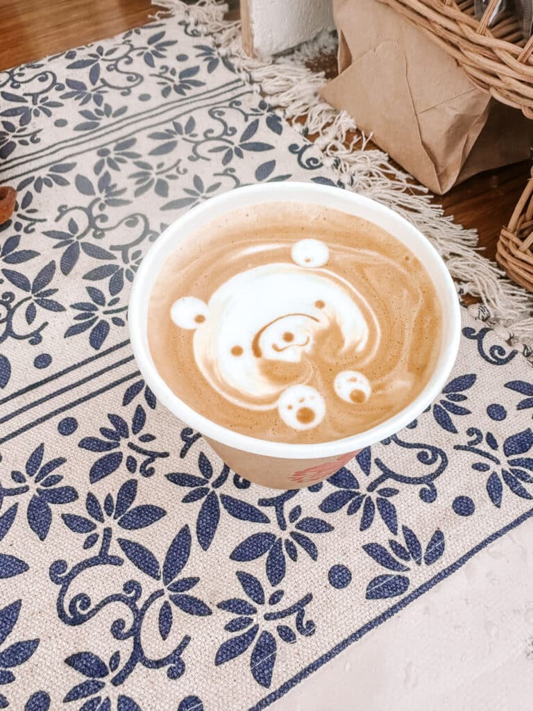 Overhead shot of a bear-shaped latte art coffee on a blue patterned cloth at Beans Coffee, Asahikawa Winter Festival.