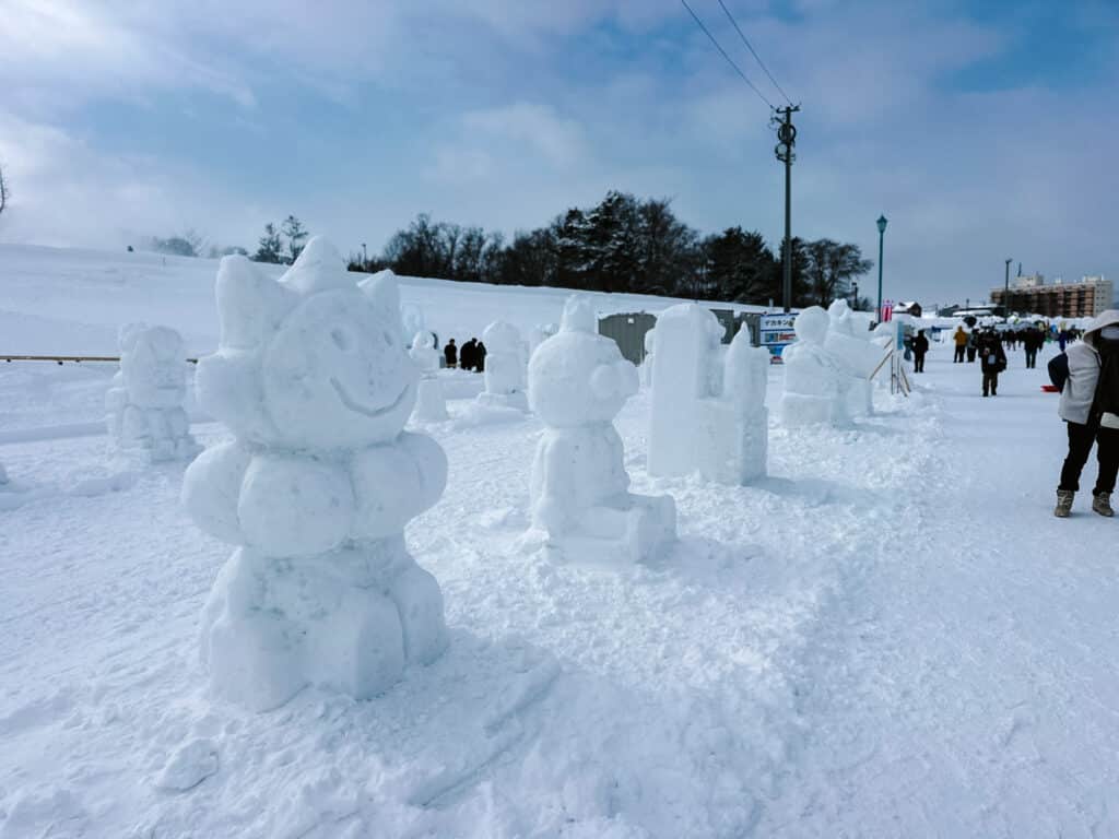 Row of cute character snow sculptures lined up across the snowy grounds of Asahikawa Winter Festival.