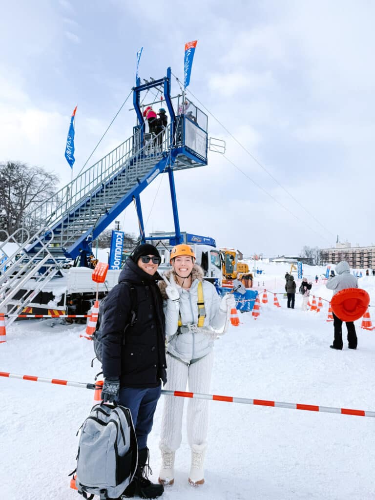 Couple wearing zipline harnesses at the base of the launch tower, ready for the Asahikawa Winter Festival zipline ride.