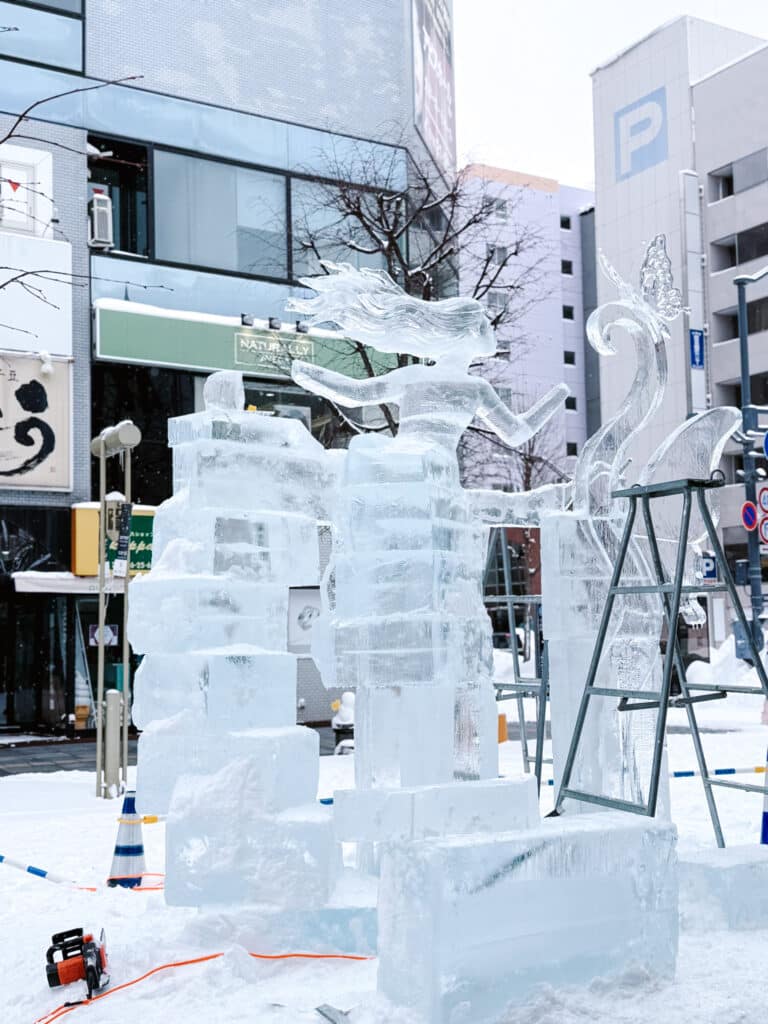Ice sculpture in progress with a stepladder beside it, on display along a downtown Asahikawa Heiwa Dori street.