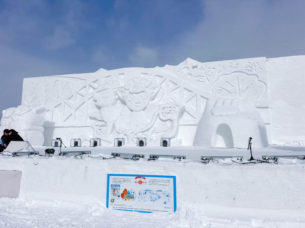 Wide view of the main Asahikawa Winter Festival snow stage featuring large carved Vulpix and Pokemon characters.
