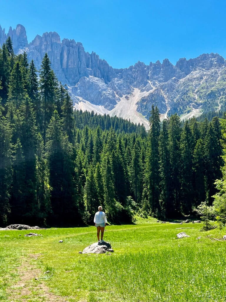 Woman standing on a rock in a green alpine meadow with the Latemar massif towering behind near Karersee in South Tyrol, Italy