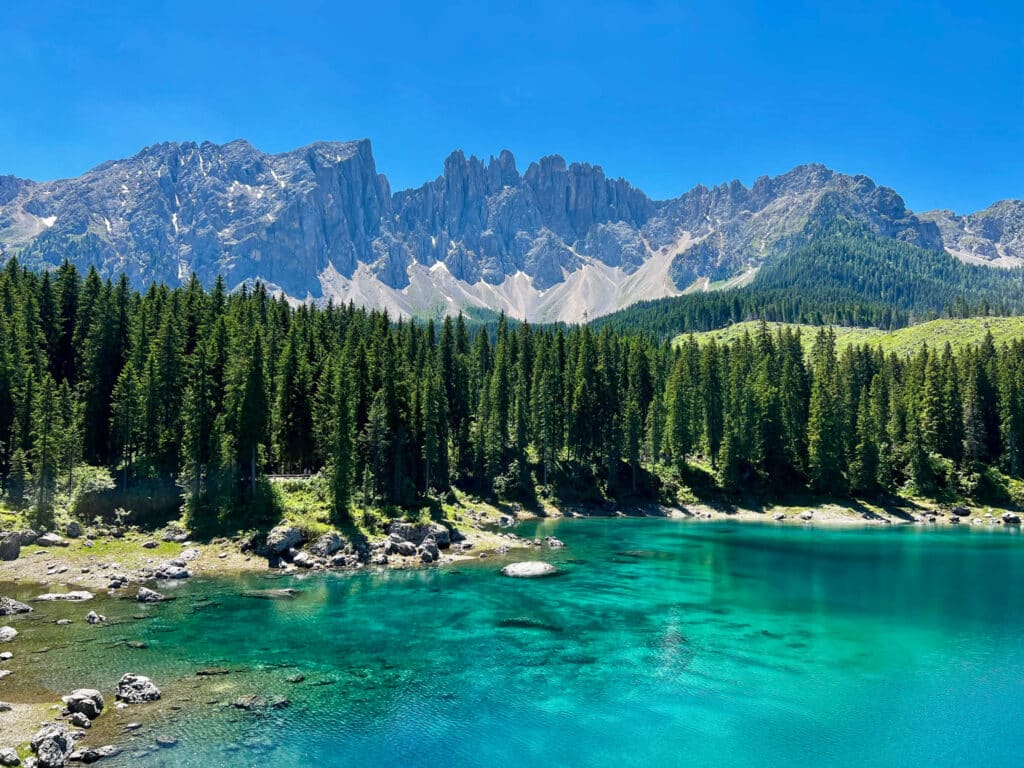 urquoise waters of Lago di Carezza (Karersee) reflecting the jagged Latemar peaks under a clear summer sky in the Italian Dolomites