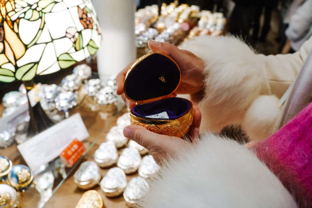 Hands opening a gold heart-shaped music box at the Otaru Music Box Museum, a stained-glass lamp glowing behind