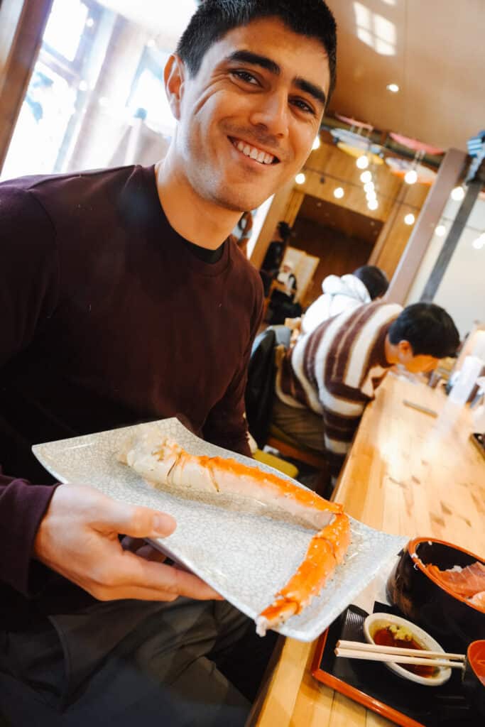 Smiling man at Donbei holding a plate with a bright orange king crab leg, Otaru's fresh Hokkaido seafood
