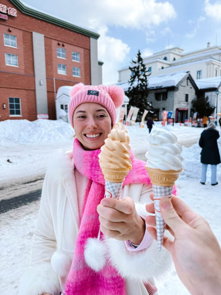 Melon and vanilla soft-serve cones clinked together outdoors in wintry Otaru, a visitor in pink smiling behind