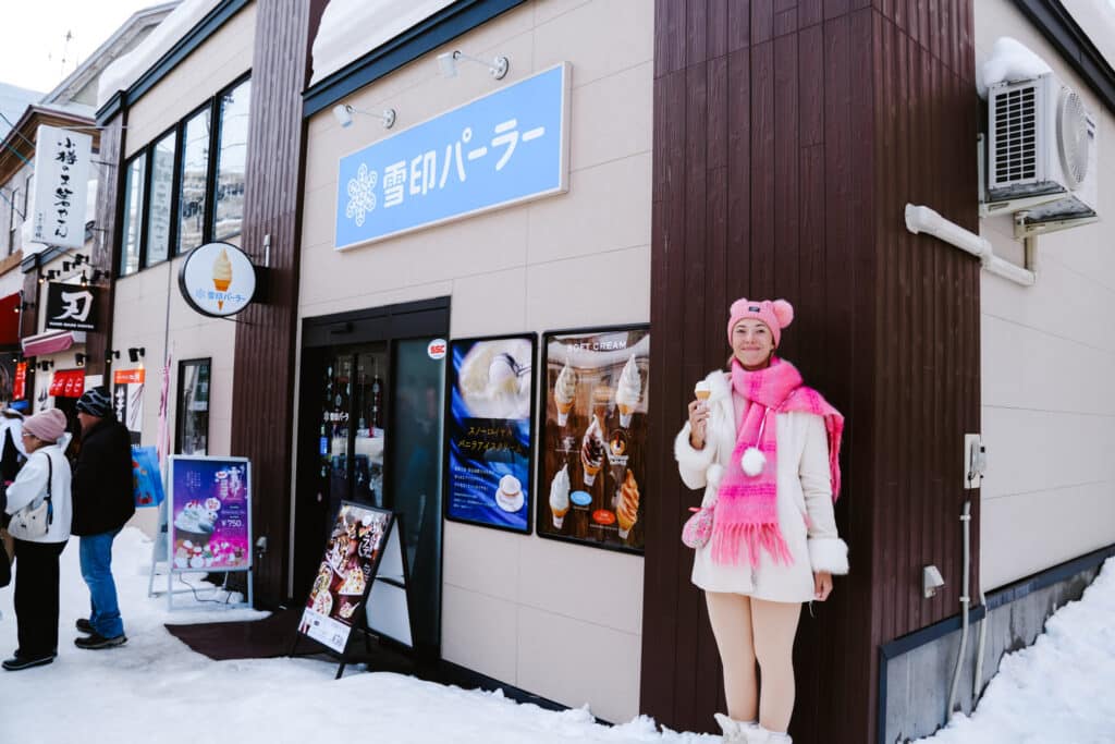 Snow Brand Parlor storefront on Sakaimachi Street, Otaru, with a visitor in pink enjoying Hokkaido milk soft serve