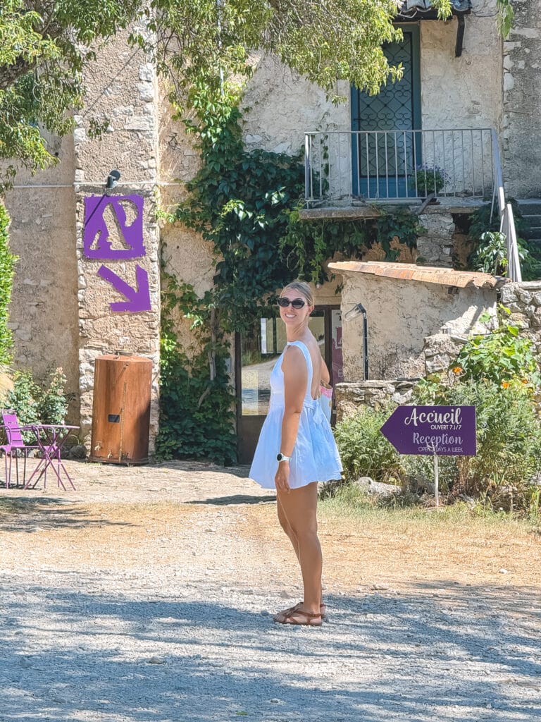 Woman in a white dress at the entrance of a Sault plateau lavender distillery with Provençal "Accueil Reception" signs