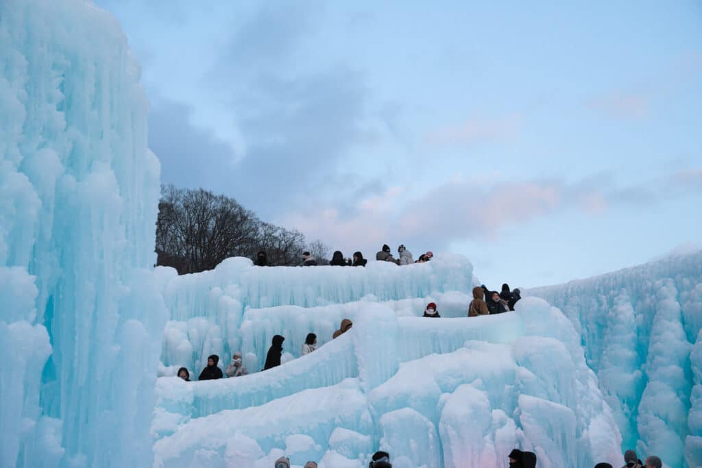 Visitors gathered atop layered ice formations against a pastel sunset sky at the Lake Shikotsu Ice Festival in Hokkaido