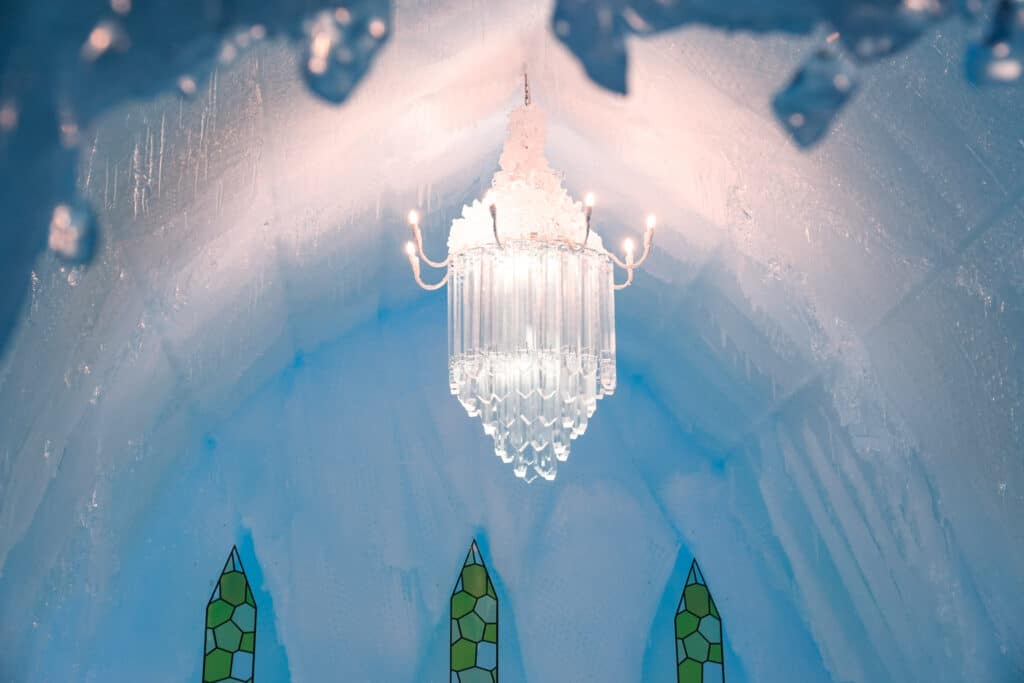Crystal chandelier glowing inside a vaulted ice chapel with green stained glass spires at the Lake Shikotsu Ice Festival