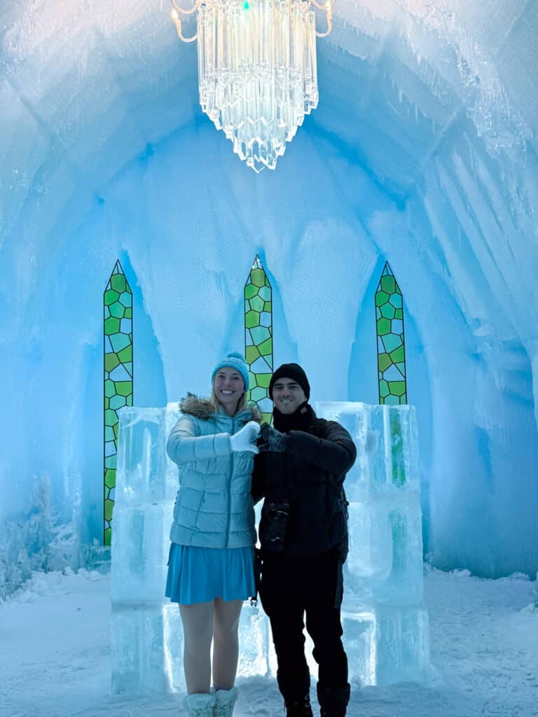 Couple making a heart with their hands beneath a crystal chandelier and green stained glass spires inside the ice chapel at Lake Shikotsu