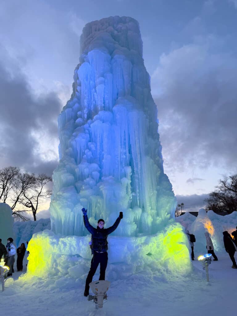Glowing blue and green ice tower lit from within against a dusky sky at the Lake Shikotsu Ice Festival, Hokkaido