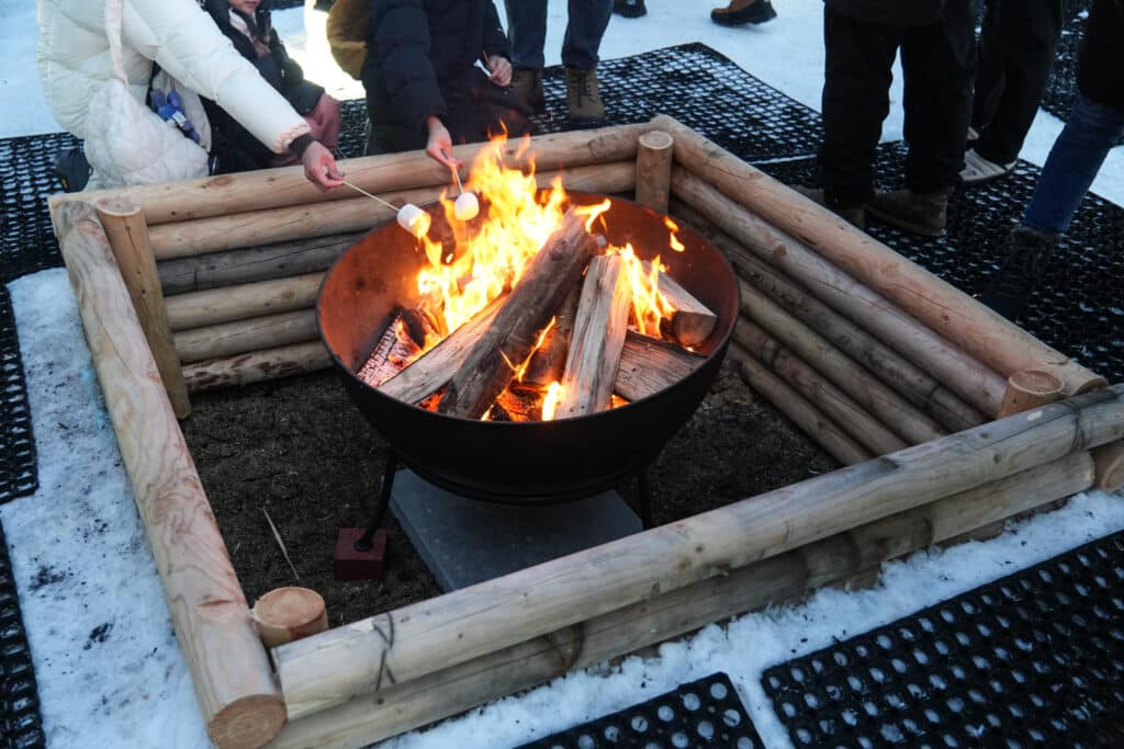 Visitor toasting marshmallows over an open fire pit ringed with logs at the Lake Shikotsu Ice Festival, Hokkaido