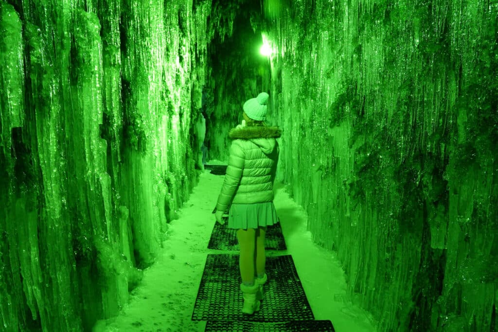 Woman in a pale silver puffer coat walking through the green-lit Mossy Forest icicle cave at the Lake Shikotsu Ice Festival, Hokkaido