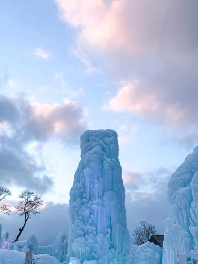 Tall pillar of dripping ice silhouetted against a soft pink and blue sunset sky at the Lake Shikotsu Ice Festival