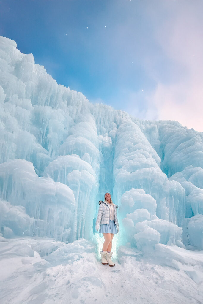 Woman in a blue skirt standing before a glowing ice wall under a starry twilight sky at the Lake Shikotsu Ice Festival