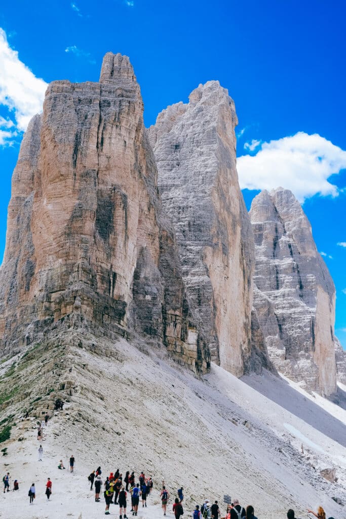 Crowd of hikers gathered at the base of the Tre Cime di Lavaredo north face, showing the scale of the towers