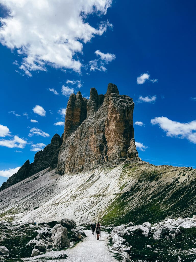 Solo hiker on a stony path approaching one of the Tre Cime di Lavaredo towers in the Italian Dolomites in summer