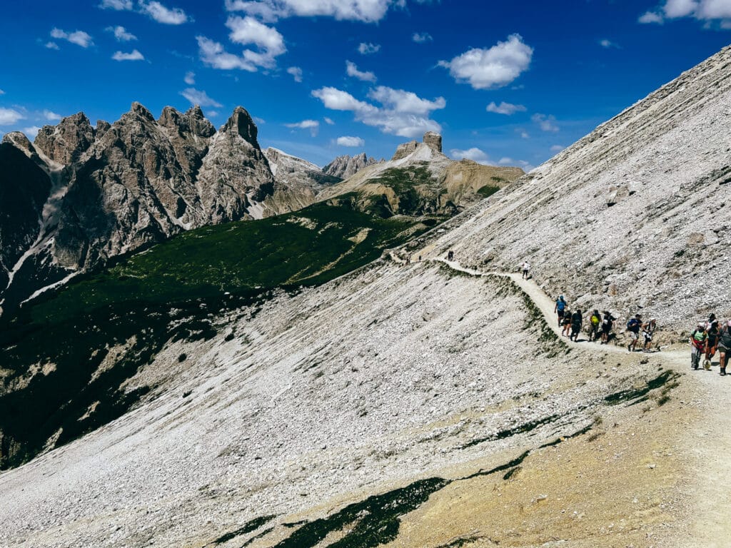 Line of hikers traversing a narrow scree path beneath rocky Dolomite peaks on the Tre Cime di Lavaredo circuit in summer