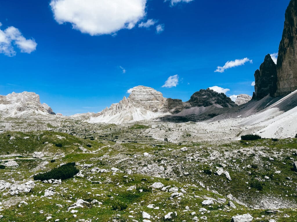 Wide view of a green Dolomite valley with the Tre Cime di Lavaredo massif rising in the background under a bright blue sky