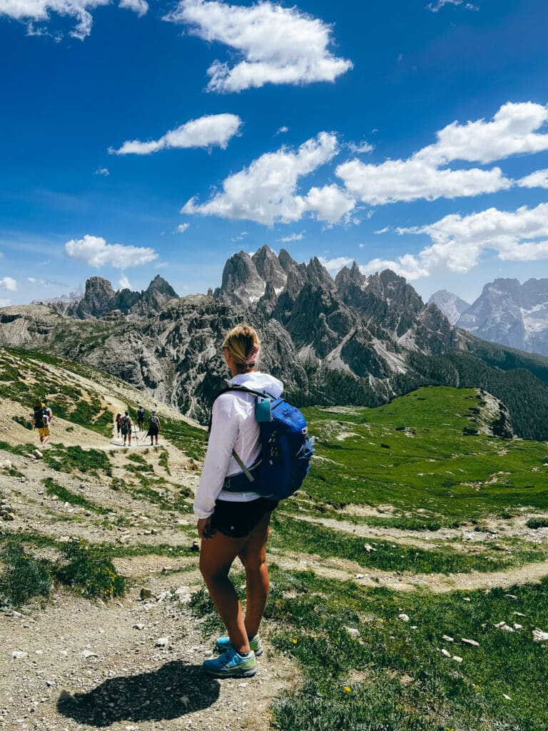 Female hiker with a blue backpack pausing on the Tre Cime di Lavaredo trail to take in the Cadini di Misurina peaks in summer