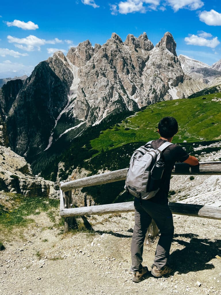Male hiker leaning on a wooden fence overlooking a sheer limestone valley along the Tre Cime di Lavaredo loop trail in summer