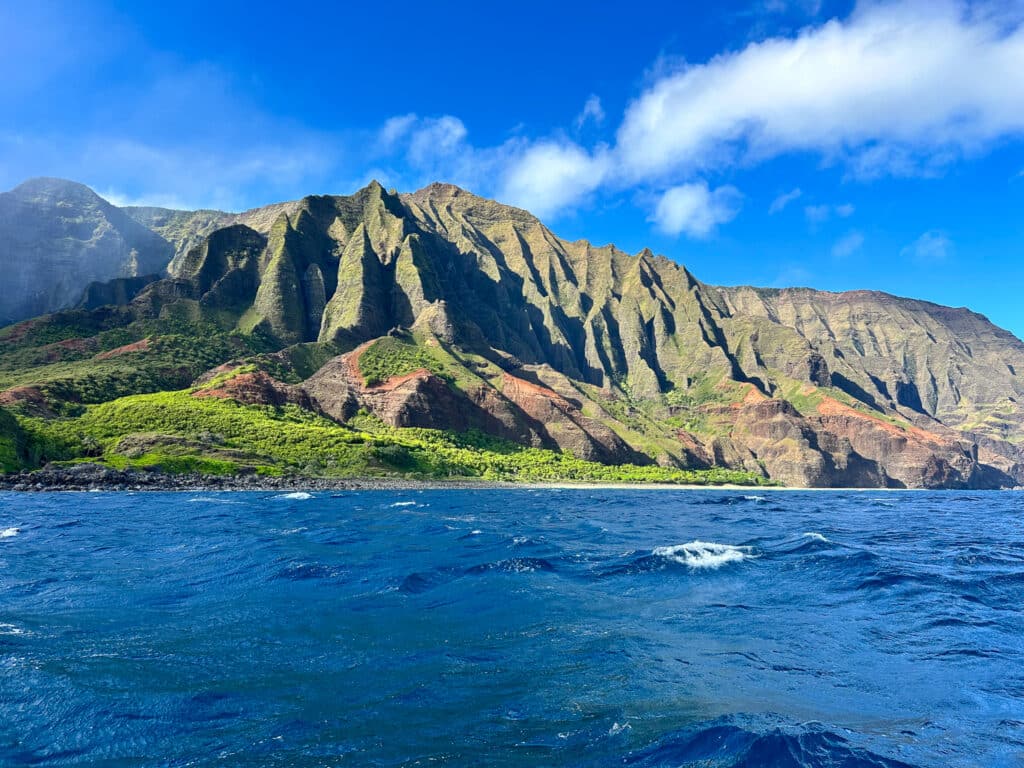 Wide amphitheater of green Na Pali ridges and red rock above choppy ocean near Kalalau, Kauai, Hawaii