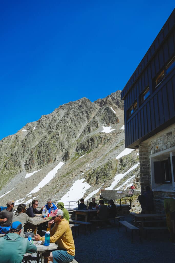 Hikers and mountaineers eating at picnic tables on the Refuge Albert Premier terrace below a rocky peak, Chamonix, France