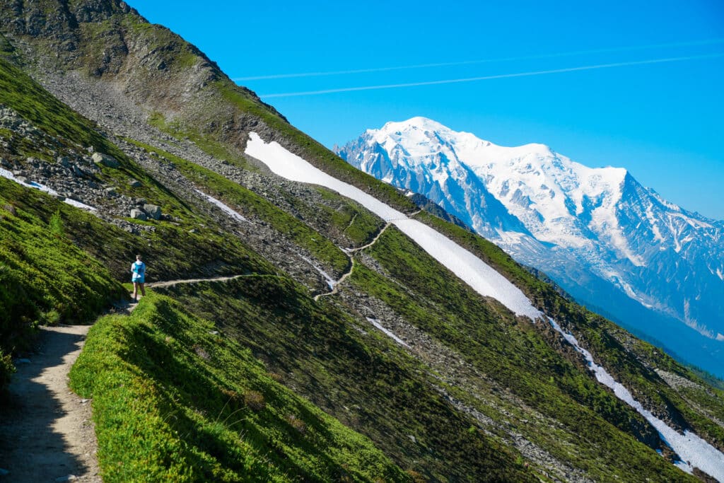 Hiker on a green traverse trail with the Mont Blanc massif in the distance, Chamonix, France