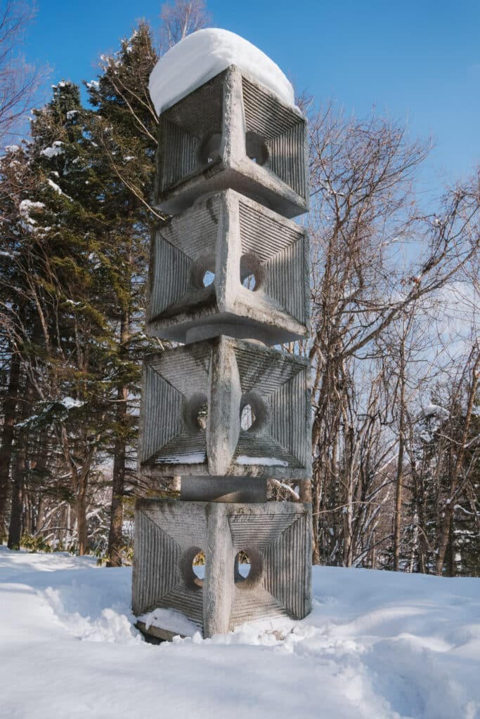 Stacked concrete cube tower sculpture capped with snow against a bright blue winter sky at Sapporo Art Park