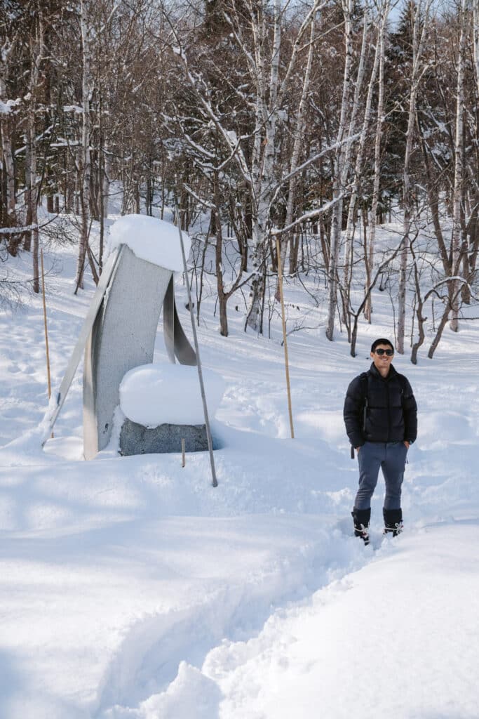 Visitor standing beside a snow-draped tent-shaped sculpture on the snowshoe trail at Sapporo Art Park, Hokkaido