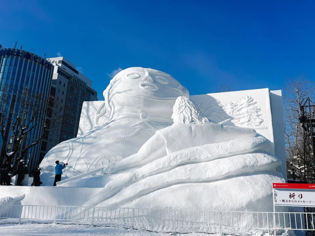 Large reclining figure snow sculpture titled "Prayer" on the Odori Park stage at the Sapporo Snow Festival, Japan