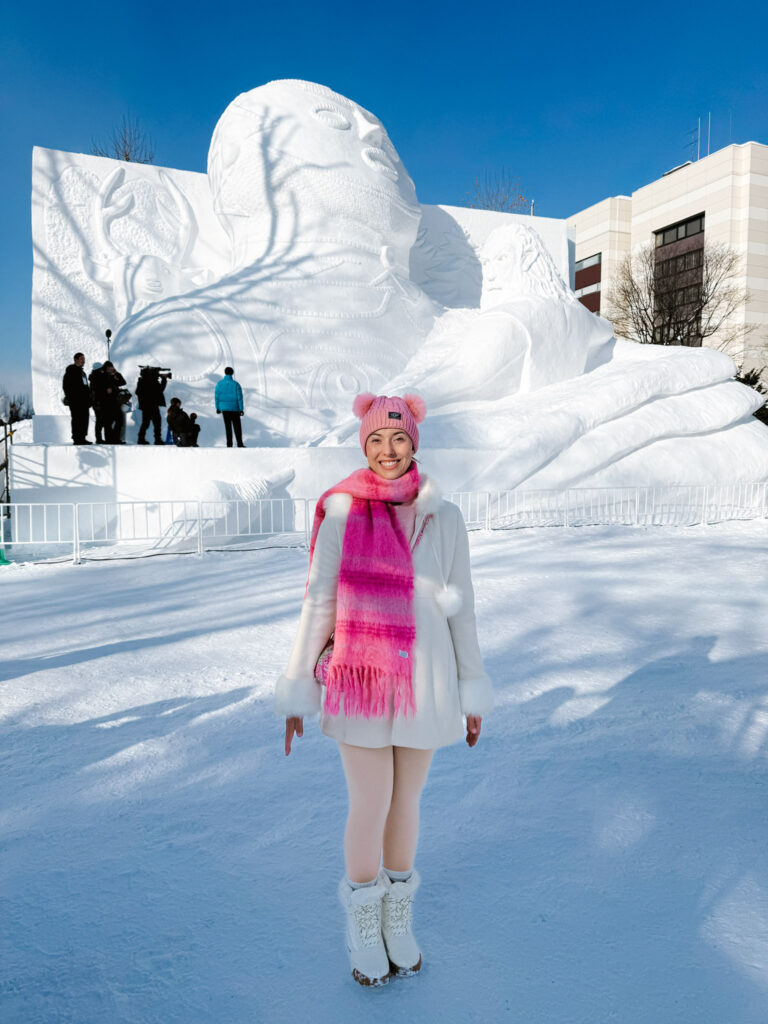 Visitor in a pink scarf in front of the towering "Prayer" snow sculpture at Odori Park, Sapporo Snow Festival, Japan