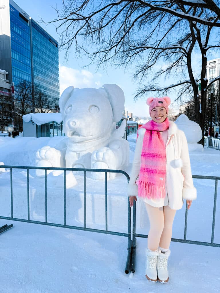 Visitor beside a friendly dog snow sculpture in low winter sun at the Sapporo Snow Festival, Hokkaido, Japan