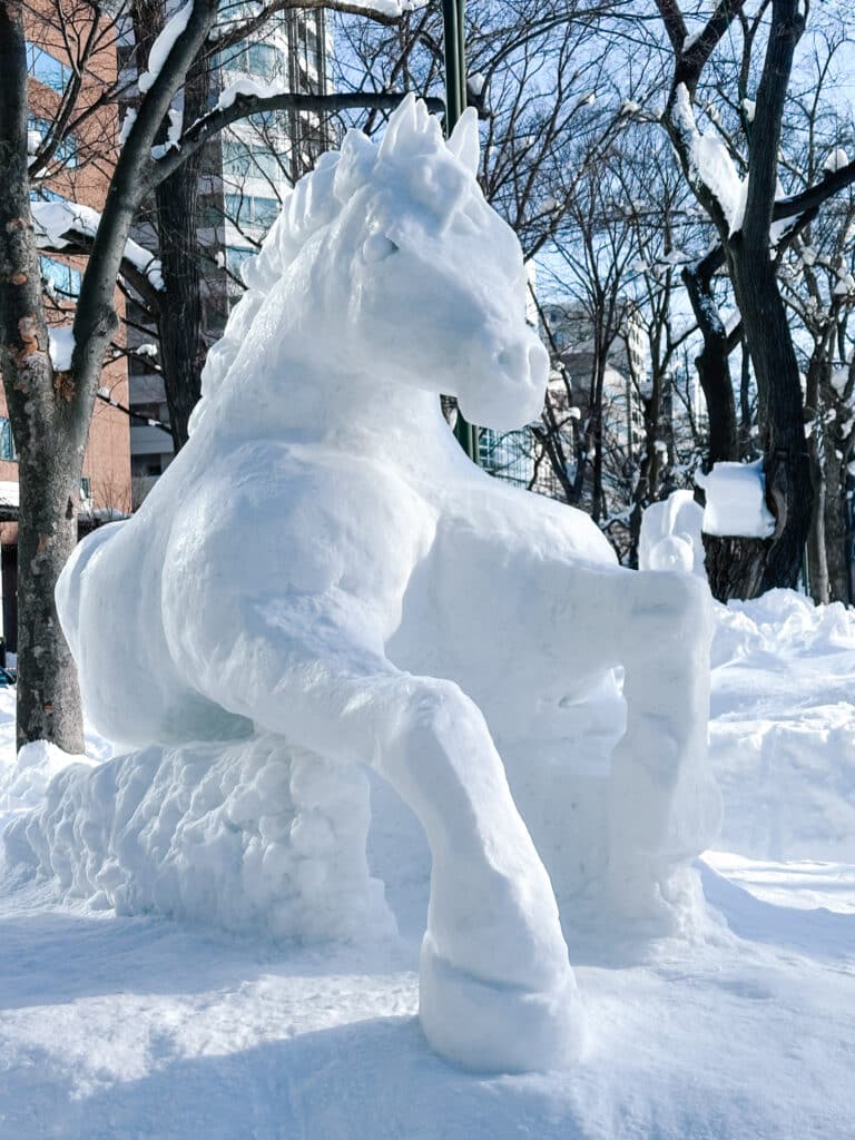 Rearing horse carved from packed snow among bare winter trees at the Sapporo Snow Festival, Hokkaido, Japan