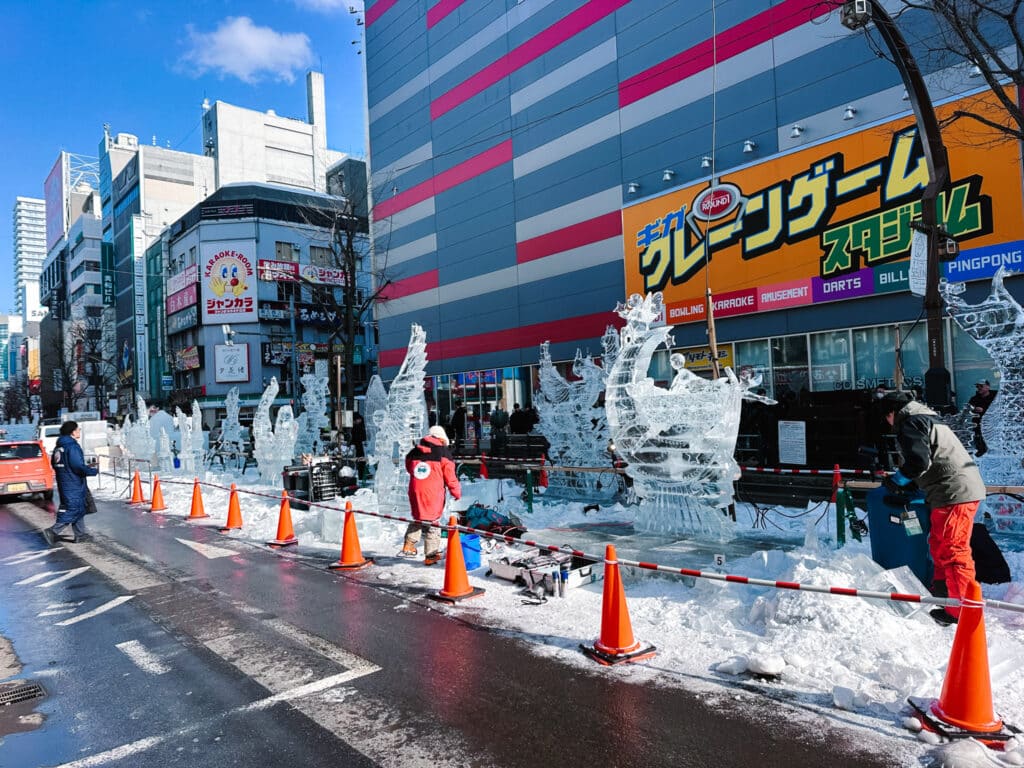 Row of ice sculptures lining the street with crew and safety cones during Susukino Ice World setup, Sapporo, Japan