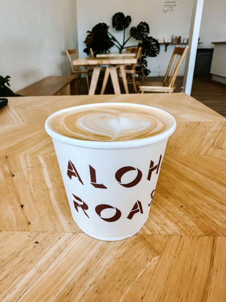 Cappuccino with heart latte art in an Aloha Roastery cup on a wood table at the specialty coffee shop near Wailua, Kauai