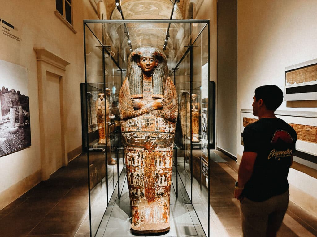 Visitor admiring a tall painted anthropoid coffin in a vaulted gallery of the Egyptian Museum in Turin