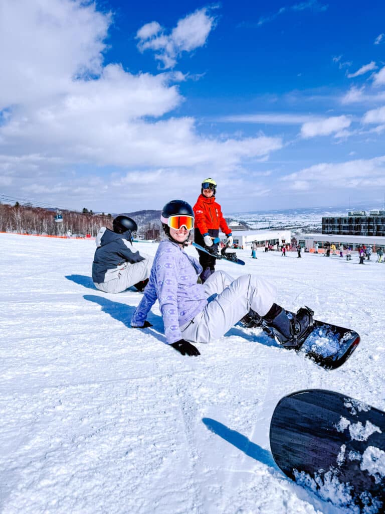 Smiling in helmet and goggles on the flats at Kitanomine during a beginner snowboard lesson in Furano