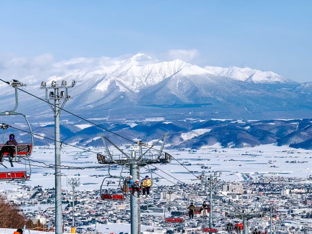Red chairlifts at Furano Ski Resort climbing above the town, Tokachi mountain range across the valley