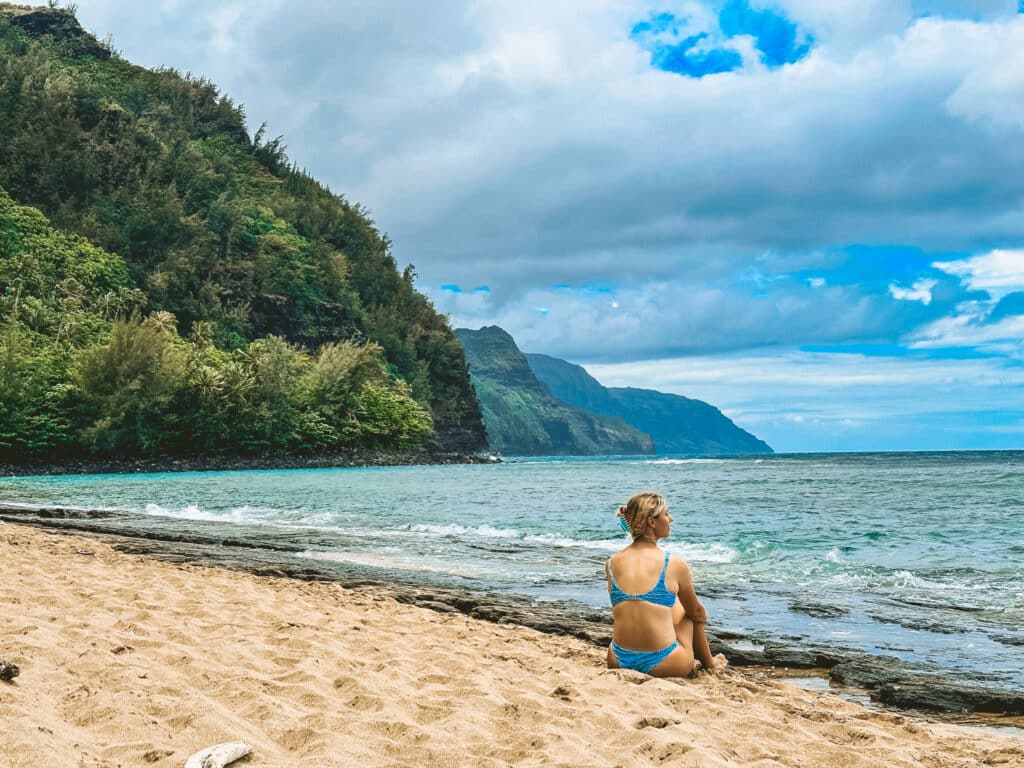 Woman sitting on Keʻe Beach taking in the Nā Pali Coast cliffs, Hāʻena State Park, Kauaʻi