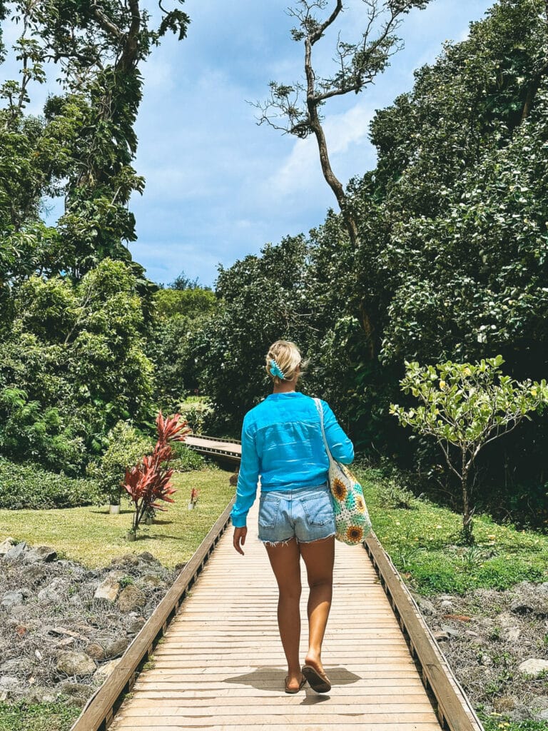 Woman in a blue top walking the boardwalk through Hāʻena State Park toward Keʻe Beach, Kauaʻi