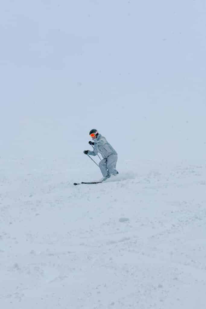 Skier kicking up fresh powder mid-turn in whiteout conditions at Furano Ski Resort, Hokkaido