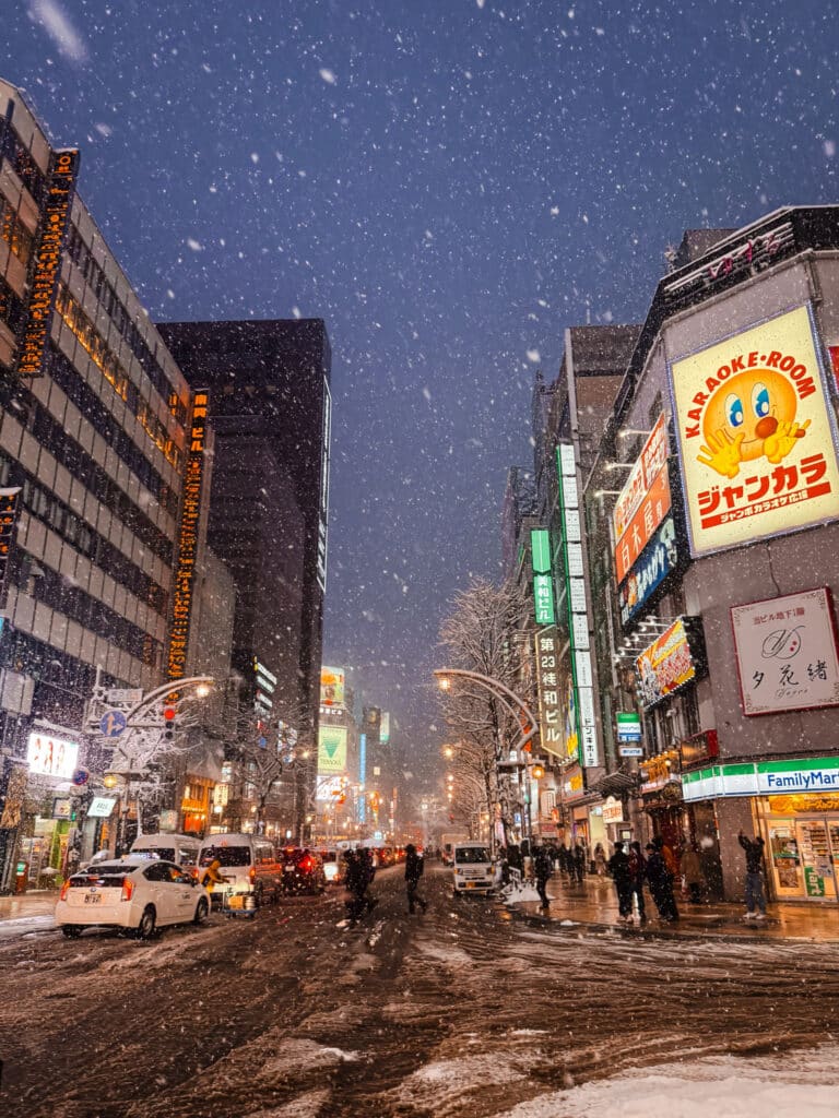 Heavy snow falling over a neon-lit city street in Susukino, Sapporo at night.